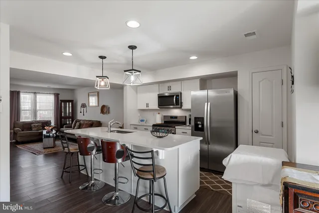 a kitchen with stainless steel appliances kitchen island granite countertop a dining table chairs refrigerator and sink