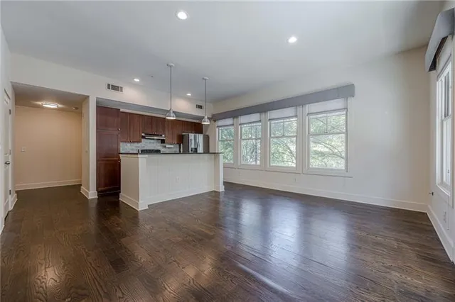 an empty room with wooden floor and a kitchen