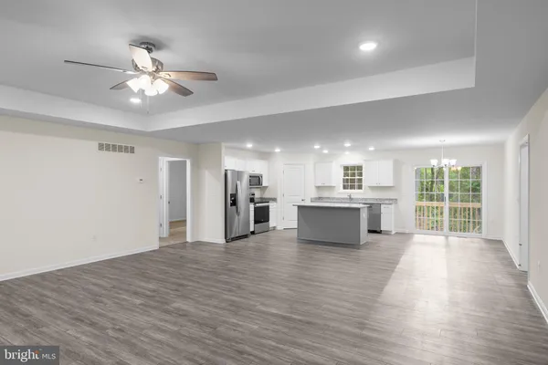 a view of an empty room with wooden floor and a kitchen