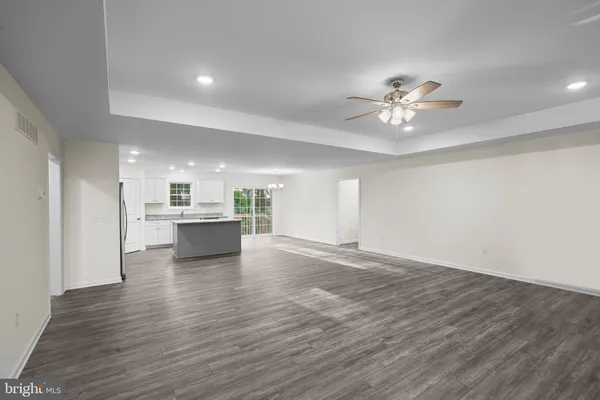 a view of an empty room and kitchen with wooden floor