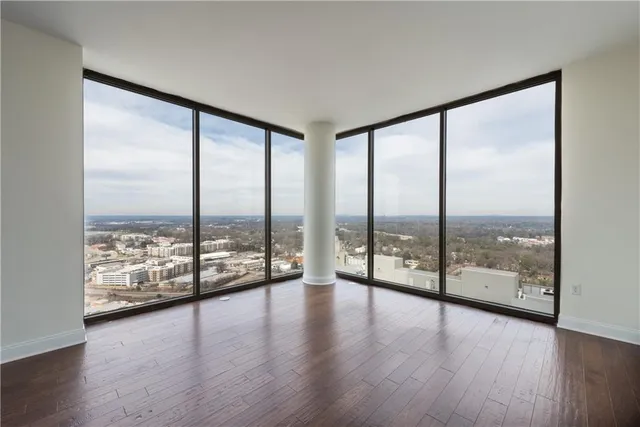 a view of an empty room with wooden floor and next to a large window