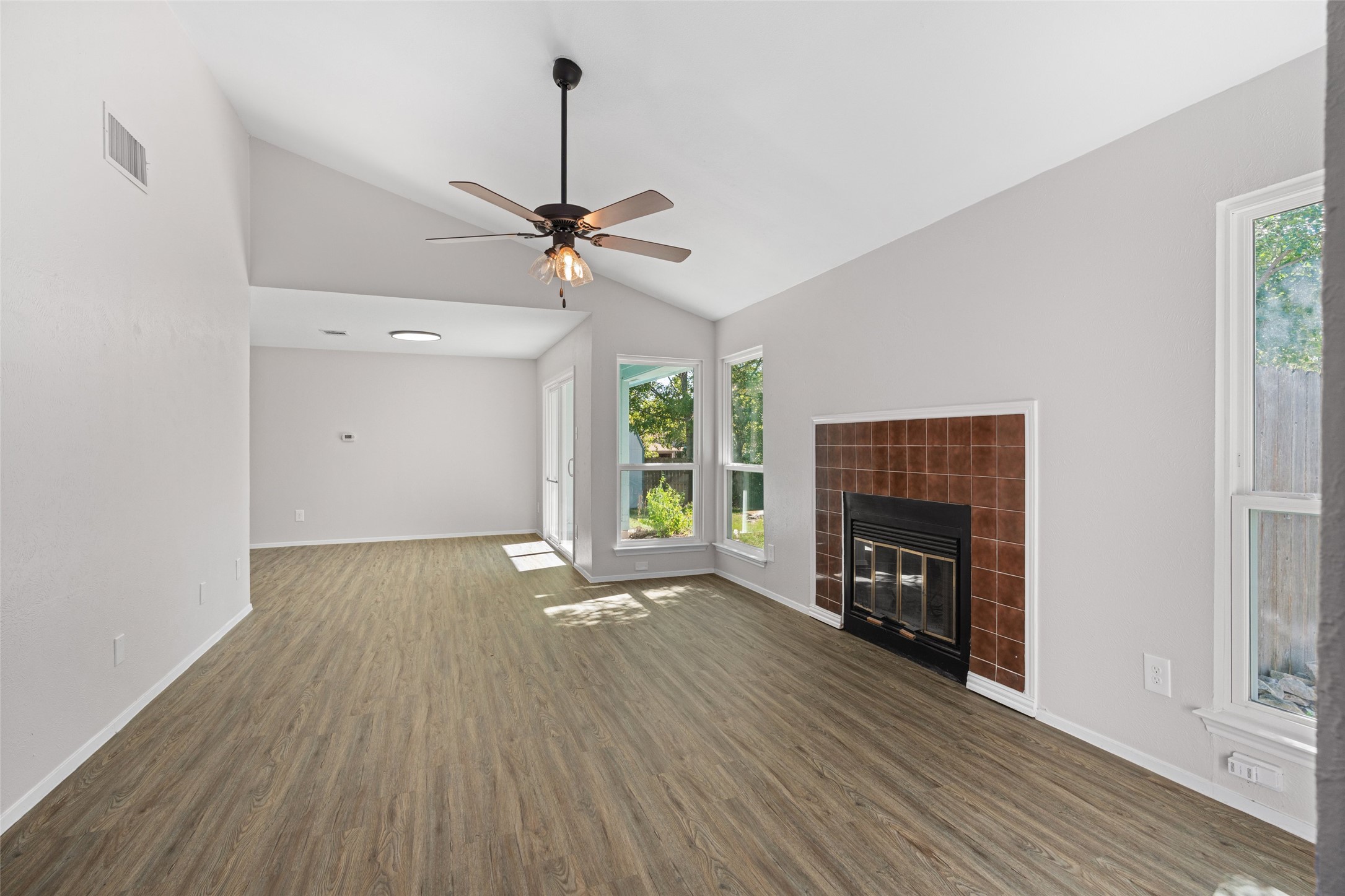 Unfurnished living room featuring dark wood-style floors, a tiled fireplace, ceiling fan, and high vaulted ceiling