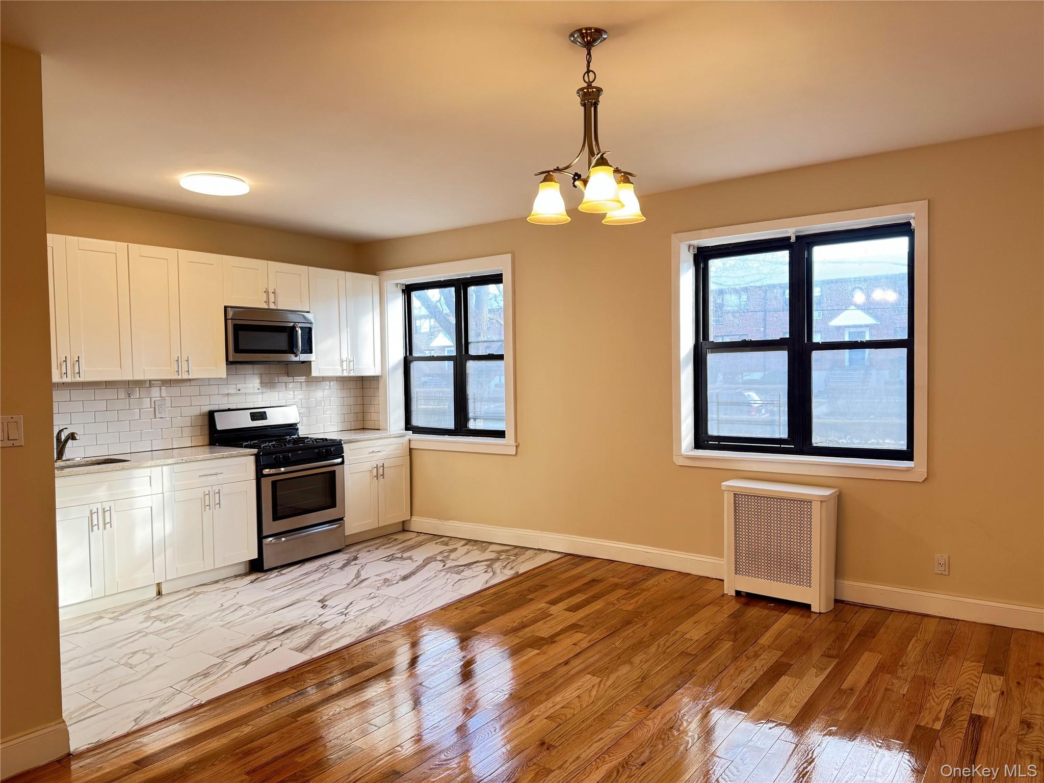 110 Stonelea Place, Unit 1B New Rochelle, NY 10801 - Photo 4 of 6 Open-concept kitchen and living area featuring white shaker cabinetry, stainless steel appliances, white subway tile backsplash, and a mixed flooring of wood-finish and patterned tile