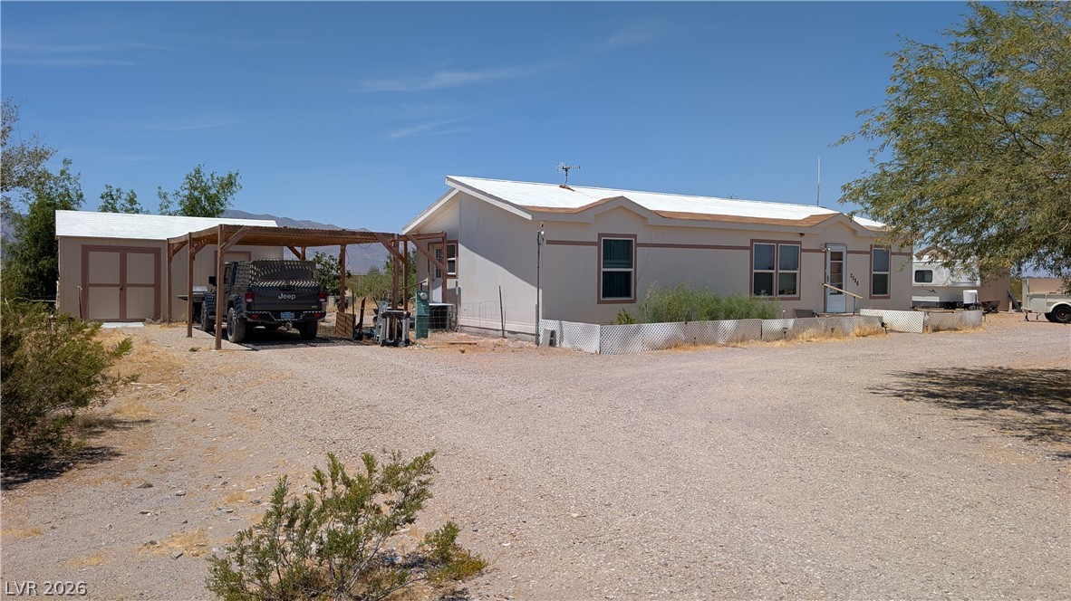 2586 South Miner Road Amargosa Valley, NV 89020 - Photo 2 of 10 A desert-landscape home features a detached shed and a spacious carport for multiple vehicles.