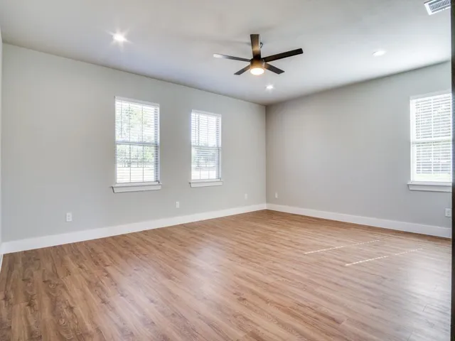 an empty room with wooden floor fan and windows