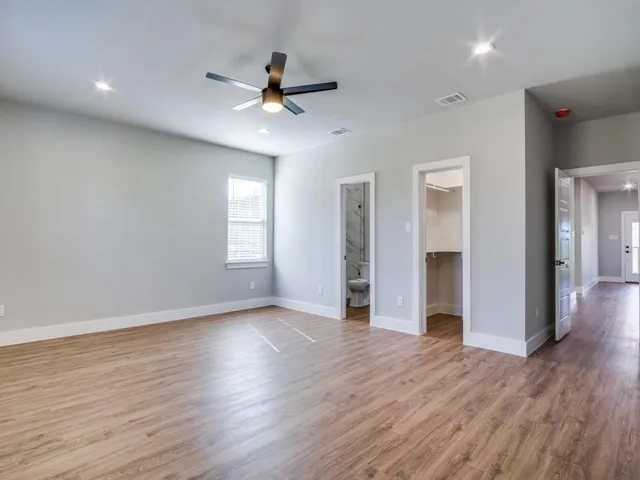 a view of an empty room with wooden floor and a ceiling fan