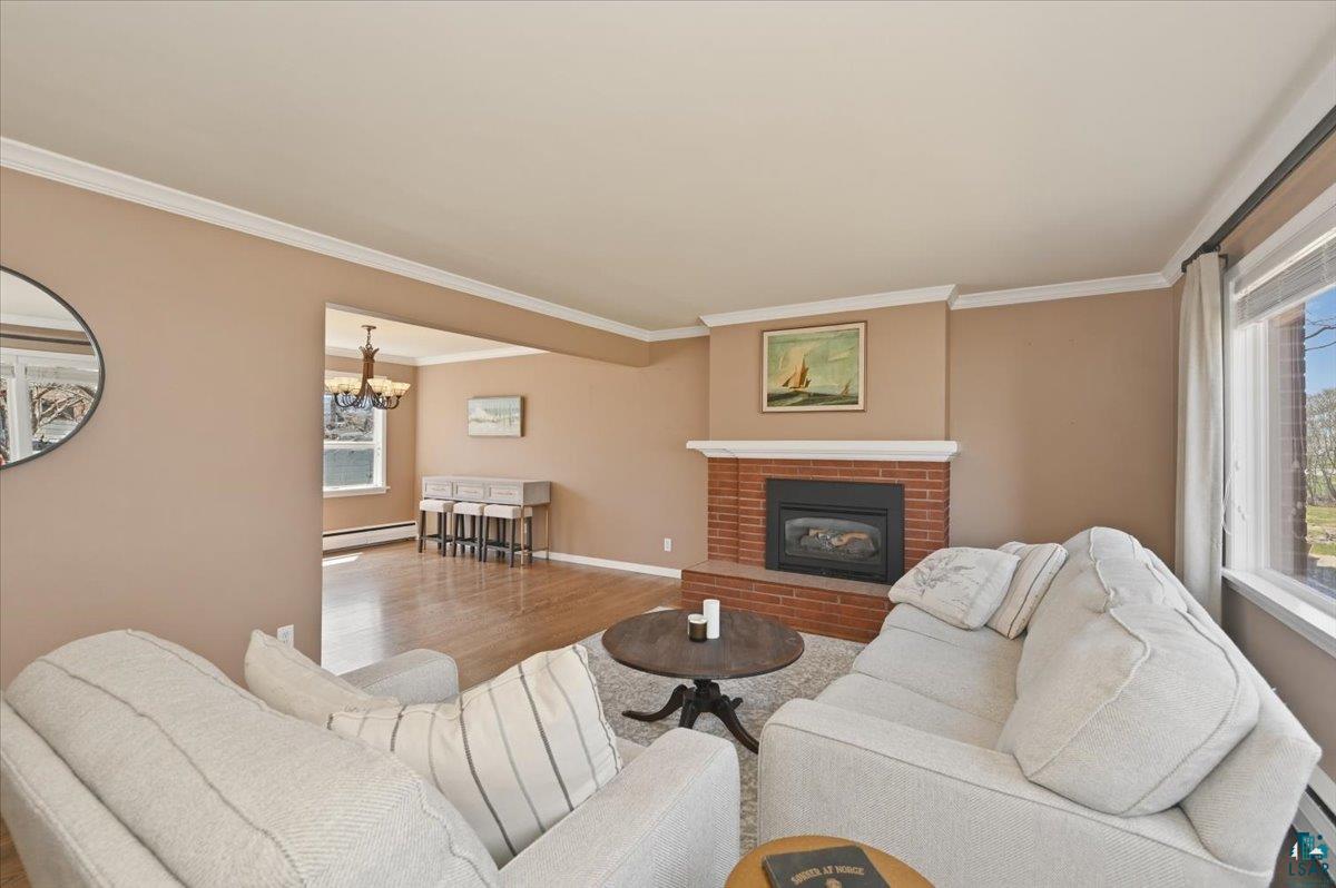 1918 West Kent Road Duluth, MN 55812 - Photo 14 of 42 Living area featuring a brick-surround fireplace with a white mantel, wood-finish flooring, and crown molding