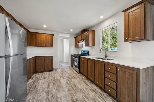 a kitchen with stainless steel appliances granite countertop a refrigerator a sink dishwasher a stove with wooden cabinets and floor