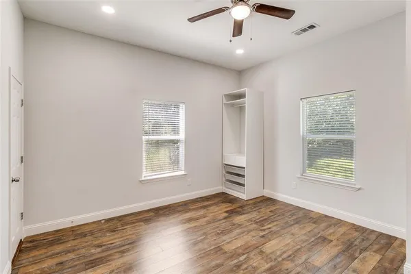 an empty room with wooden floor chandelier fan and windows