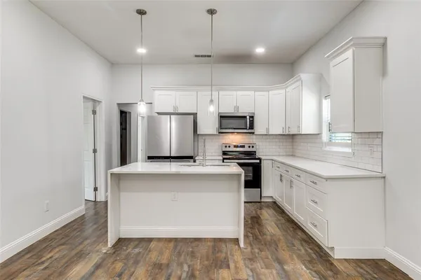 a kitchen with kitchen island a white counter top space stainless steel appliances and cabinets