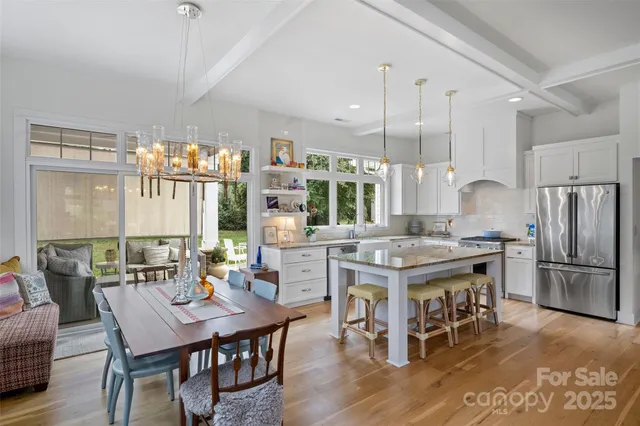 a kitchen with stainless steel appliances granite countertop a stove a refrigerator a kitchen island a dining table and chairs with wooden floor