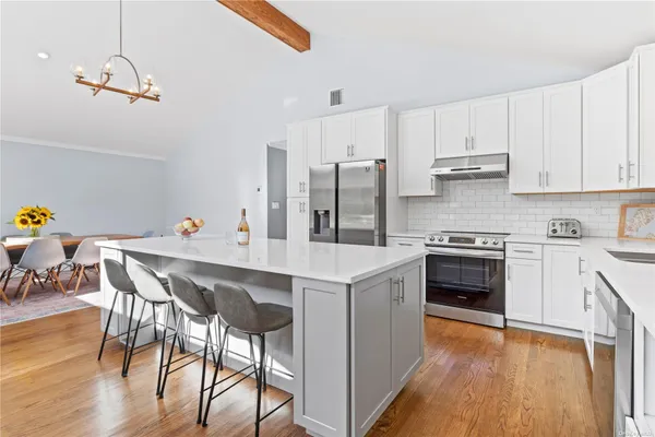 a kitchen with stainless steel appliances a stove a sink dishwasher a refrigerator white cabinets and wooden floor