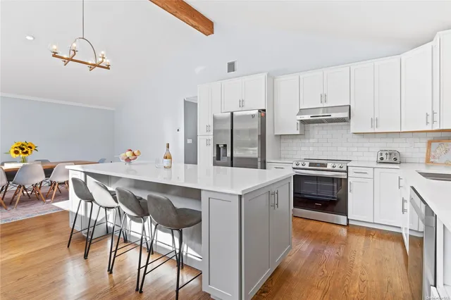 a kitchen with stainless steel appliances a stove a sink dishwasher a refrigerator white cabinets and wooden floor