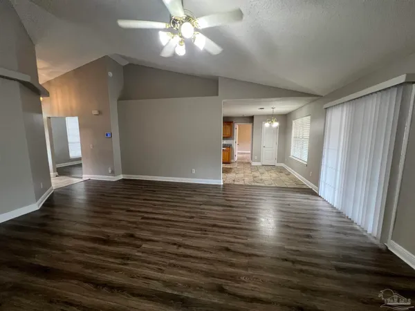 a view of an empty room with wooden floor and a kitchen