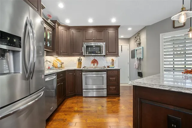 a kitchen with stainless steel appliances kitchen island granite countertop a refrigerator a stove a sink dishwasher and a dining table with wooden floor
