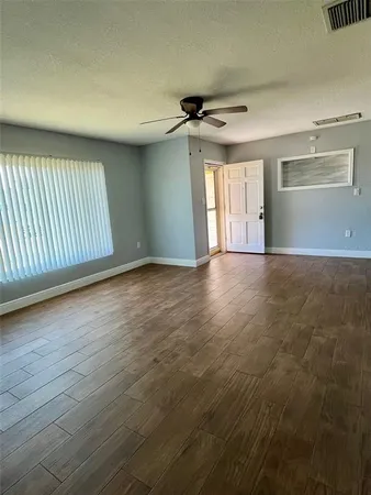 an empty room with wooden floor ceiling fan and windows