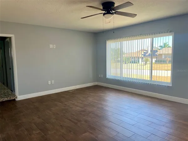 an empty room with wooden floor fan and windows