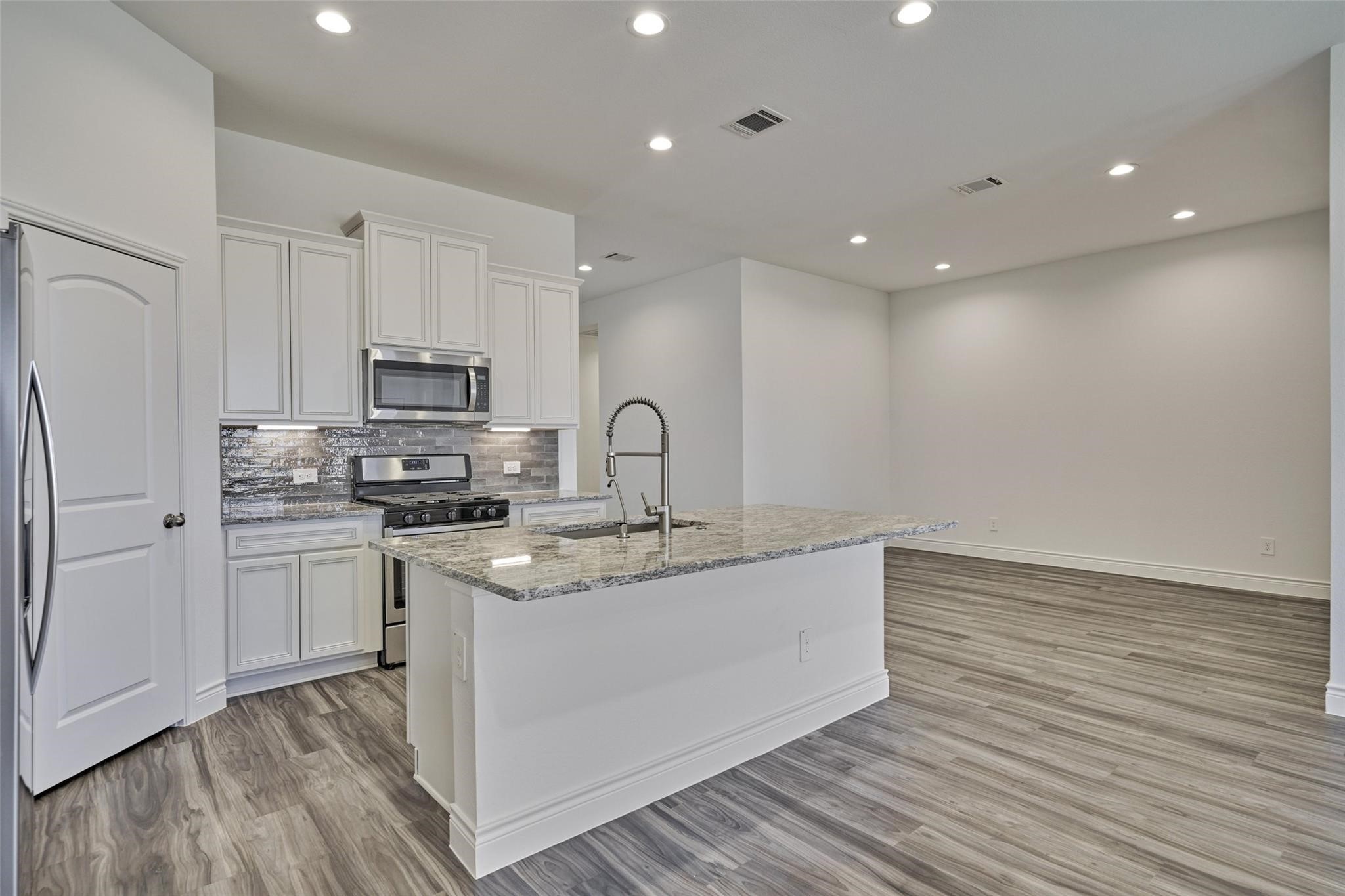 981 Youth Water Road Montgomery, TX 77316 - Photo 19 of 43 a kitchen with stainless steel appliances granite countertop a sink stove refrigerator and white cabinets with wooden floor