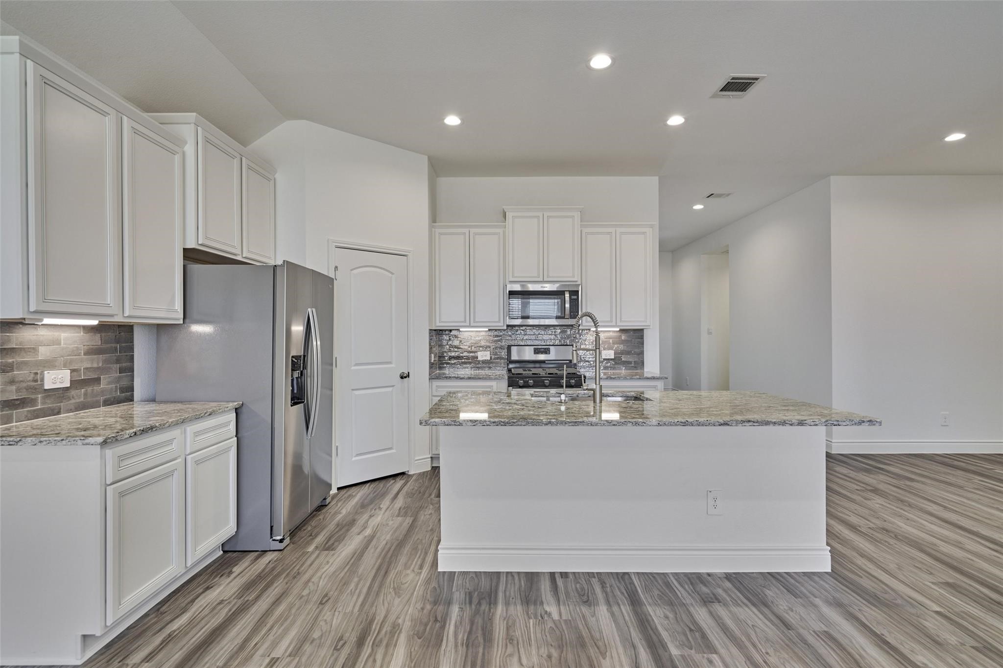 981 Youth Water Road Montgomery, TX 77316 - Photo 20 of 43 a kitchen with stainless steel appliances a refrigerator a stove and white cabinets with wooden floor
