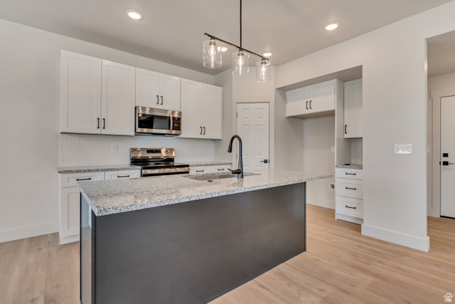2535 West Santa Fe Drive Mapleton, UT 84664 - Photo 10 of 26 Two tone kitchen with stainless steel appliances, light wood finished floors, light stone counters, hanging light fixtures, and an island with sink