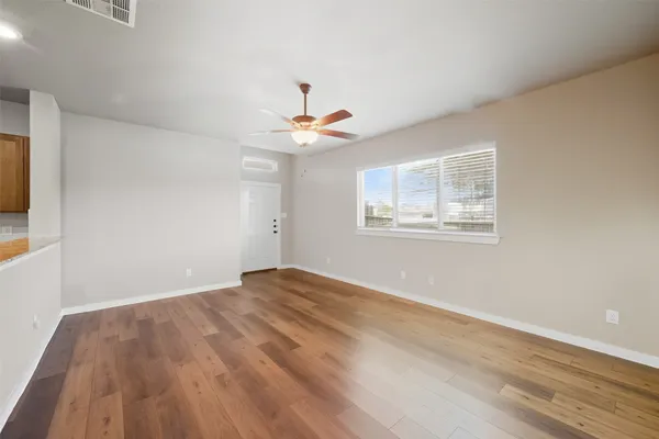 a big room with wooden floor a ceiling fan and windows