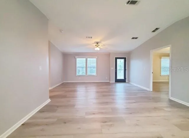 an empty room with wooden floor fan and windows