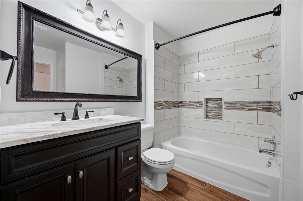 41 Abbey Road Euless, TX 76039 - Photo 19 of 23 Rich wood plank flooring coordinates with a dark vanity under contemporary tile surround.