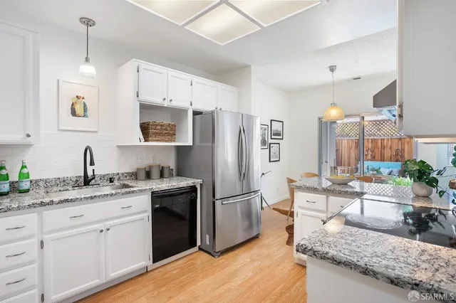 a kitchen with stainless steel appliances granite countertop a refrigerator a sink dishwasher a oven with white cabinets and wooden floor