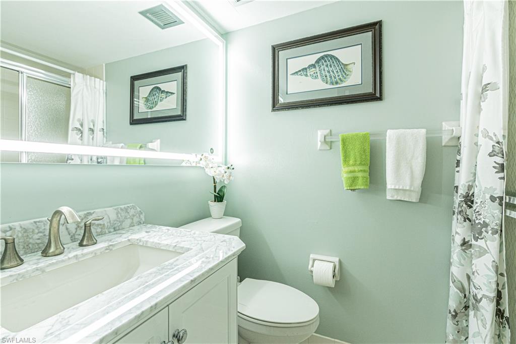1 High Point Circle West, Unit 102 Naples, FL 34103 - Photo 16 of 35 a bathroom with a granite countertop toilet sink and mirror