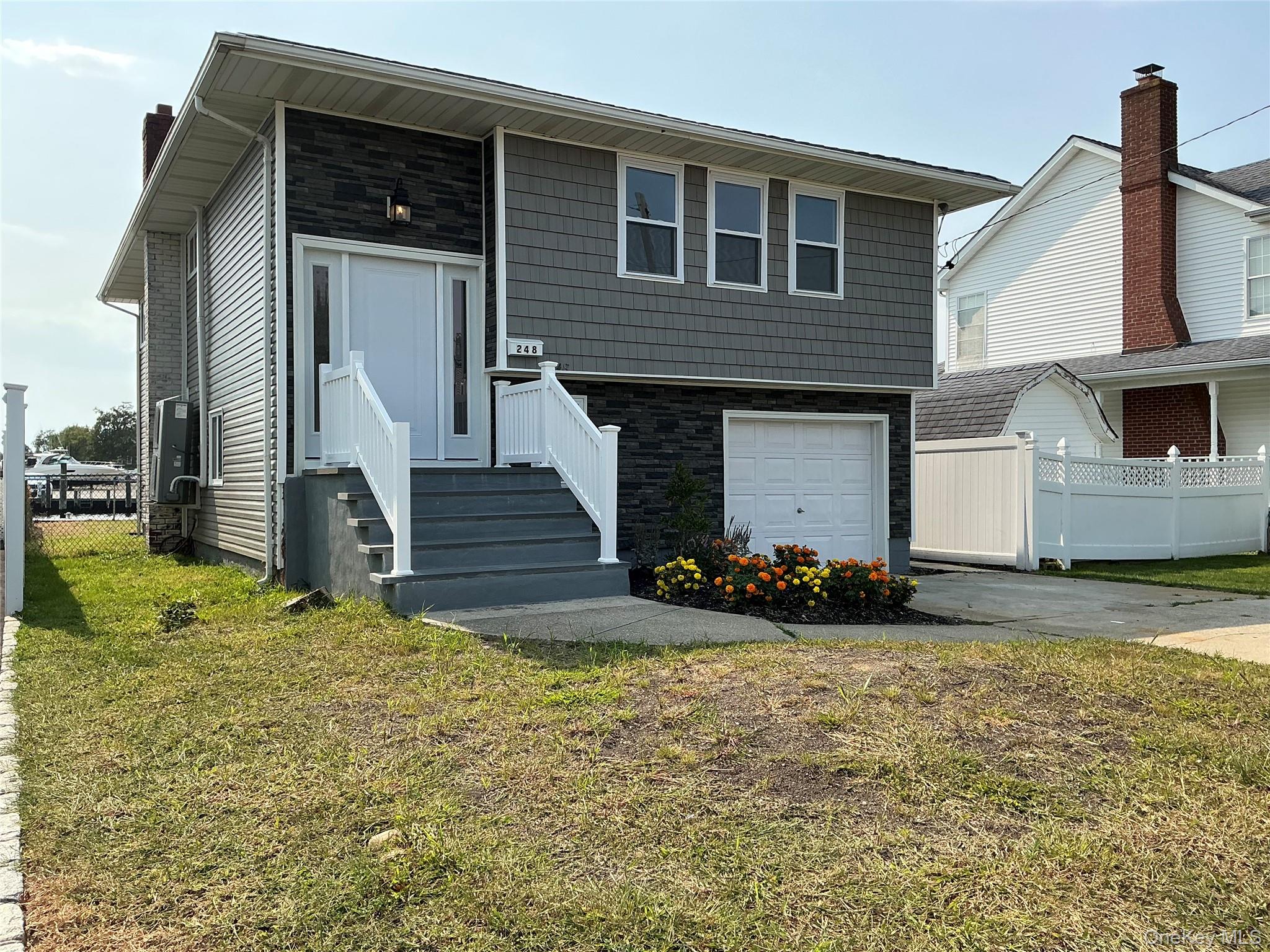 248 East Shore Road Lindenhurst, NY 11757 - Photo 2 of 46 View of front facade featuring stone siding, concrete driveway, and an attached garage