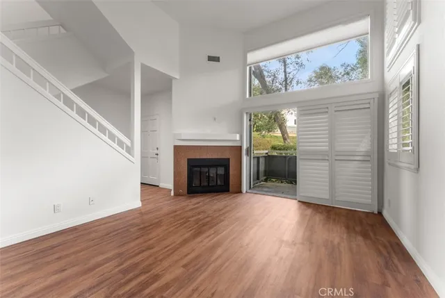 a view of an empty room with wooden floor fireplace and a window
