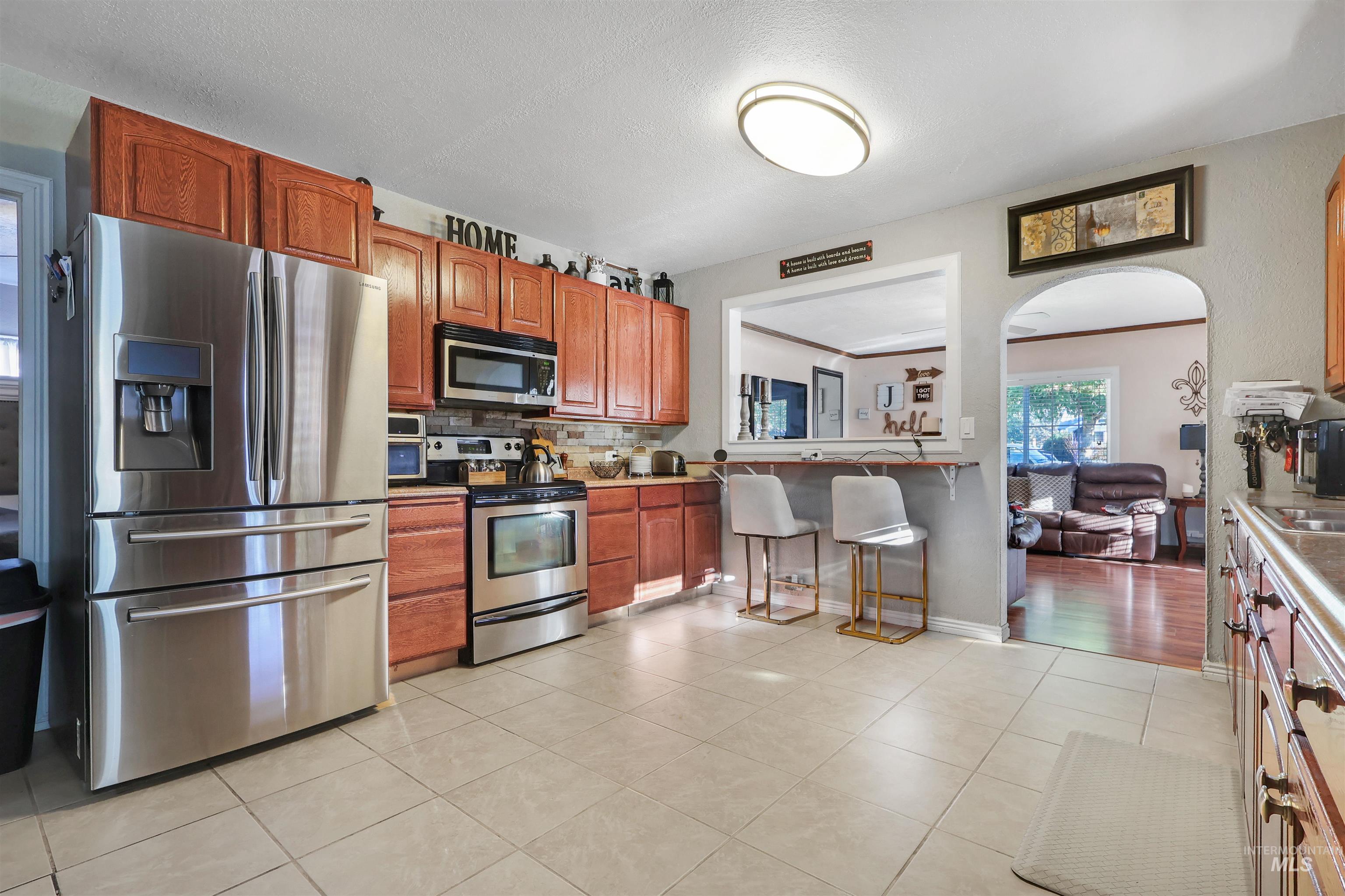 1009 9th Street Rupert, ID 83350 - Photo 7 of 28 Kitchen featuring stainless steel appliances, wood-finish cabinetry, tile flooring, and a pass-through window with a built-in counter