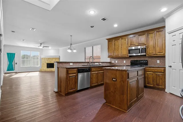 a kitchen with stainless steel appliances granite countertop wooden cabinets a refrigerator a stove a microwave and wooden floors