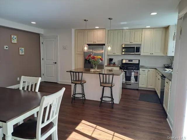 a kitchen with stainless steel appliances granite countertop a stove top oven a refrigerator a dining table and chairs with wooden floor