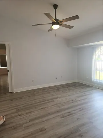 an empty room with wooden floor fan and windows