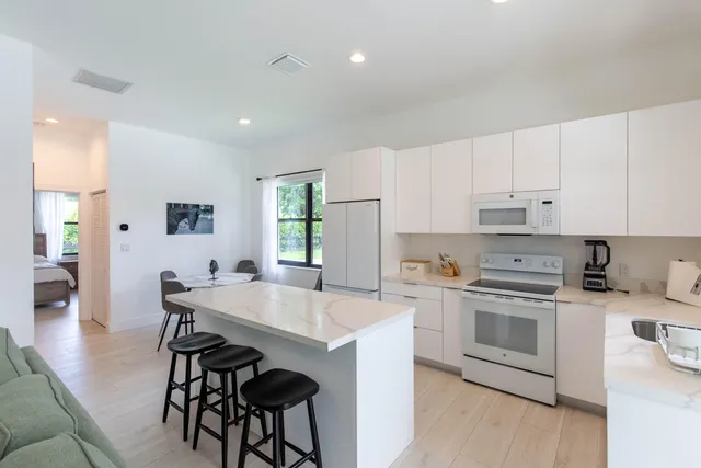 a kitchen with stainless steel appliances a stove a sink a microwave a refrigerator and white cabinets with wooden floor