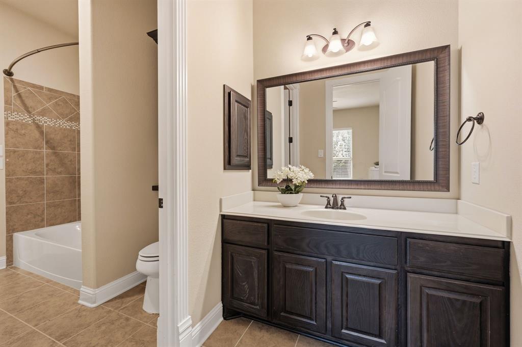 7013 Handel Colleyville, TX 76034 - Photo 26 of 37 Bathroom vanity featuring dark wood-finish cabinetry, a white countertop with an integrated sink, and a framed mirror