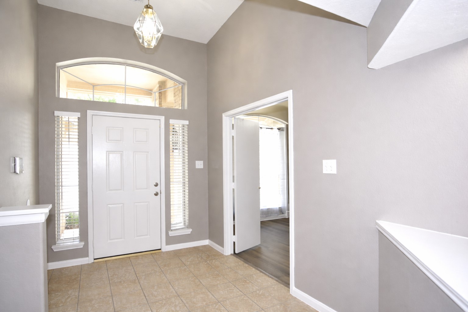 9611 Babbling Spring Court Tomball, TX 77375 - Photo 3 of 31 Bright entryway featuring high ceilings, neutral walls, and tile flooring. A white front door with side windows and a transom allows natural light. An open doorway leads to another room with wood flooring.