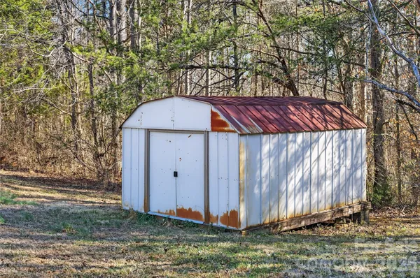 a view of a small barn with a small yard and large trees
