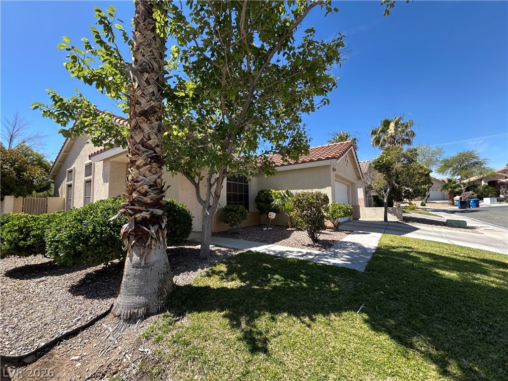 1840 Montvale Las Vegas, NV 89134 - Photo 4 of 31 A well-maintained stucco home with a terracotta tile roof and lush green landscaping.