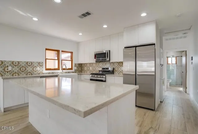 a kitchen with stainless steel appliances granite countertop a refrigerator a stove a sink a microwave a refrigerator and white cabinets with wooden floor