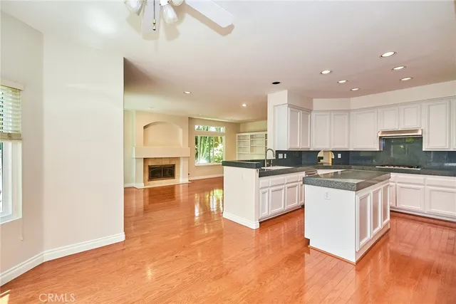 a kitchen with kitchen island granite countertop a stove a sink and white cabinets with wooden floor