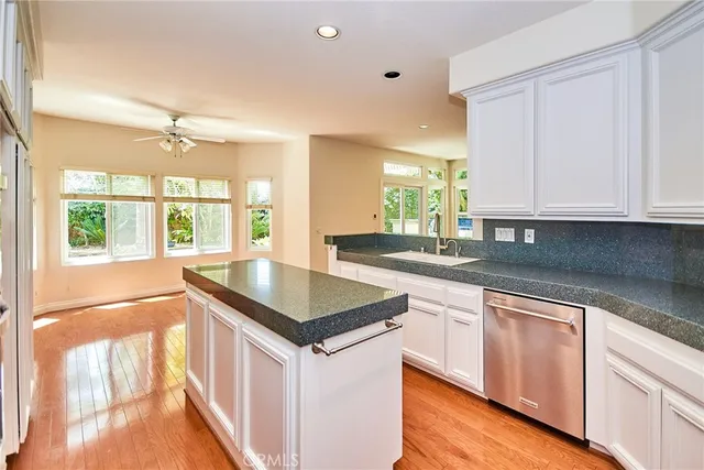 a large kitchen with stainless steel appliances granite countertop a stove a sink a refrigerator and white cabinets with wooden floor