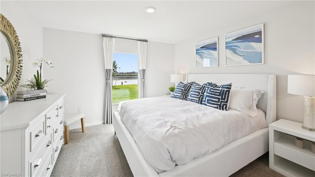 5007 3rd Street West Lehigh Acres, FL 33971 - Photo 14 of 24 Model Home. This bedroom features light-colored walls and carpeting, a window with a view of a body of water and green space, and a white dresser with a round mirror