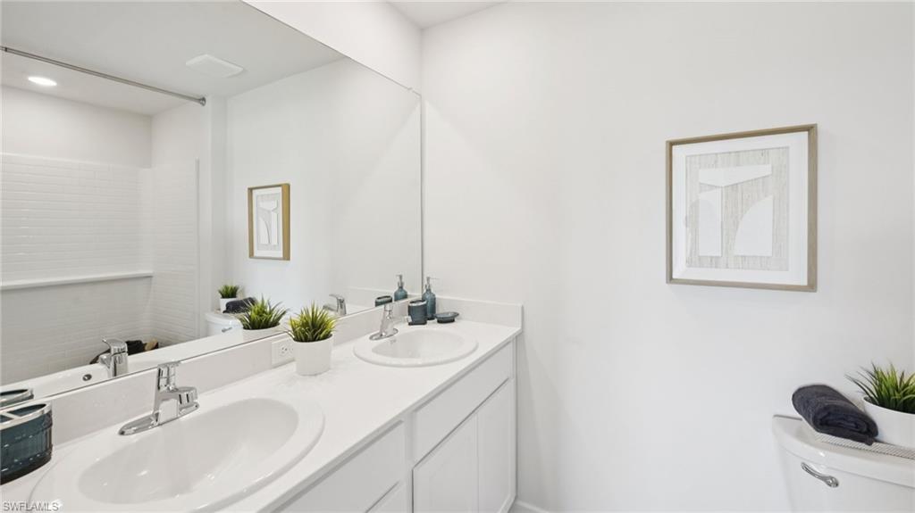 5007 3rd Street West Lehigh Acres, FL 33971 - Photo 15 of 24 Model Home. Bathroom featuring a large vanity with dual sinks and chrome faucets, a full-width mirror, and white subway tile in the shower area