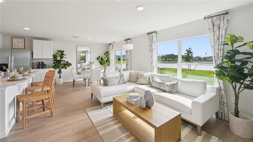 5007 3rd Street West Lehigh Acres, FL 33971 - Photo 2 of 24 Model Home. This open-concept living area features light wood-look flooring, large windows with views of the surrounding landscape, and a kitchen island with seating