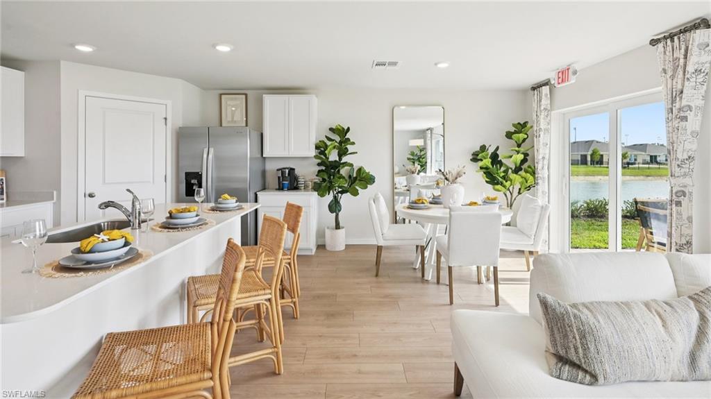 5007 3rd Street West Lehigh Acres, FL 33971 - Photo 3 of 24 Model Home. Open concept living area featuring light wood-style flooring, a kitchen island with seating, and a dining area with views of the outdoor landscape
