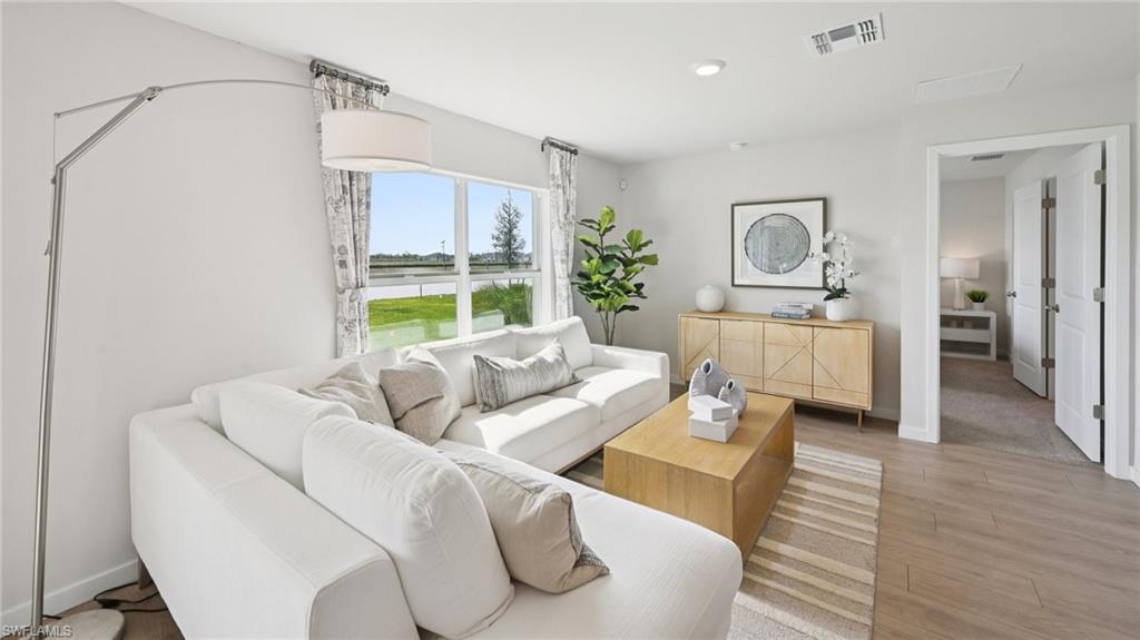 5007 3rd Street West Lehigh Acres, FL 33971 - Photo 4 of 24 Model Home. The living area features light-toned walls, wood-style flooring, and a large window providing views of the exterior