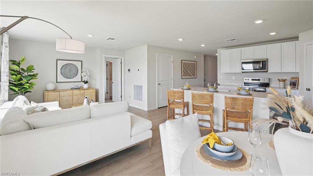 5007 3rd Street West Lehigh Acres, FL 33971 - Photo 6 of 24 Model Home. The property features an open-concept living area with light-colored flooring, a kitchen with white cabinetry and stainless steel appliances, and a breakfast bar with seating