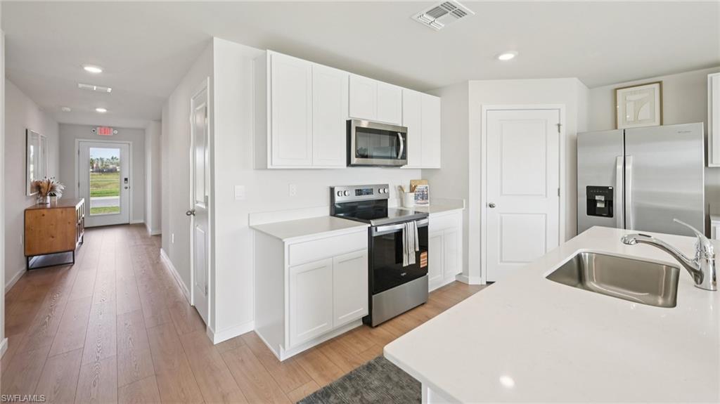 5007 3rd Street West Lehigh Acres, FL 33971 - Photo 8 of 24 Model Home. The kitchen features white cabinetry, stainless steel appliances, and a central island with an integrated sink and faucet